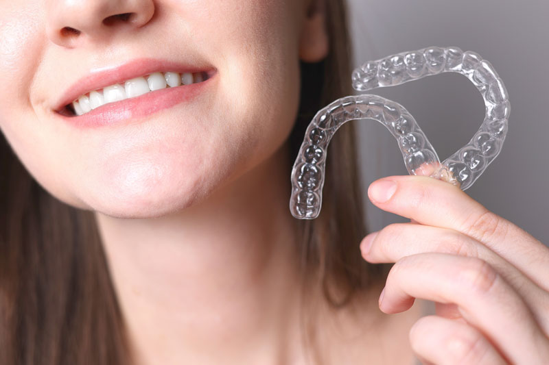 a woman holding 2 invisalign retainers and smiling widely